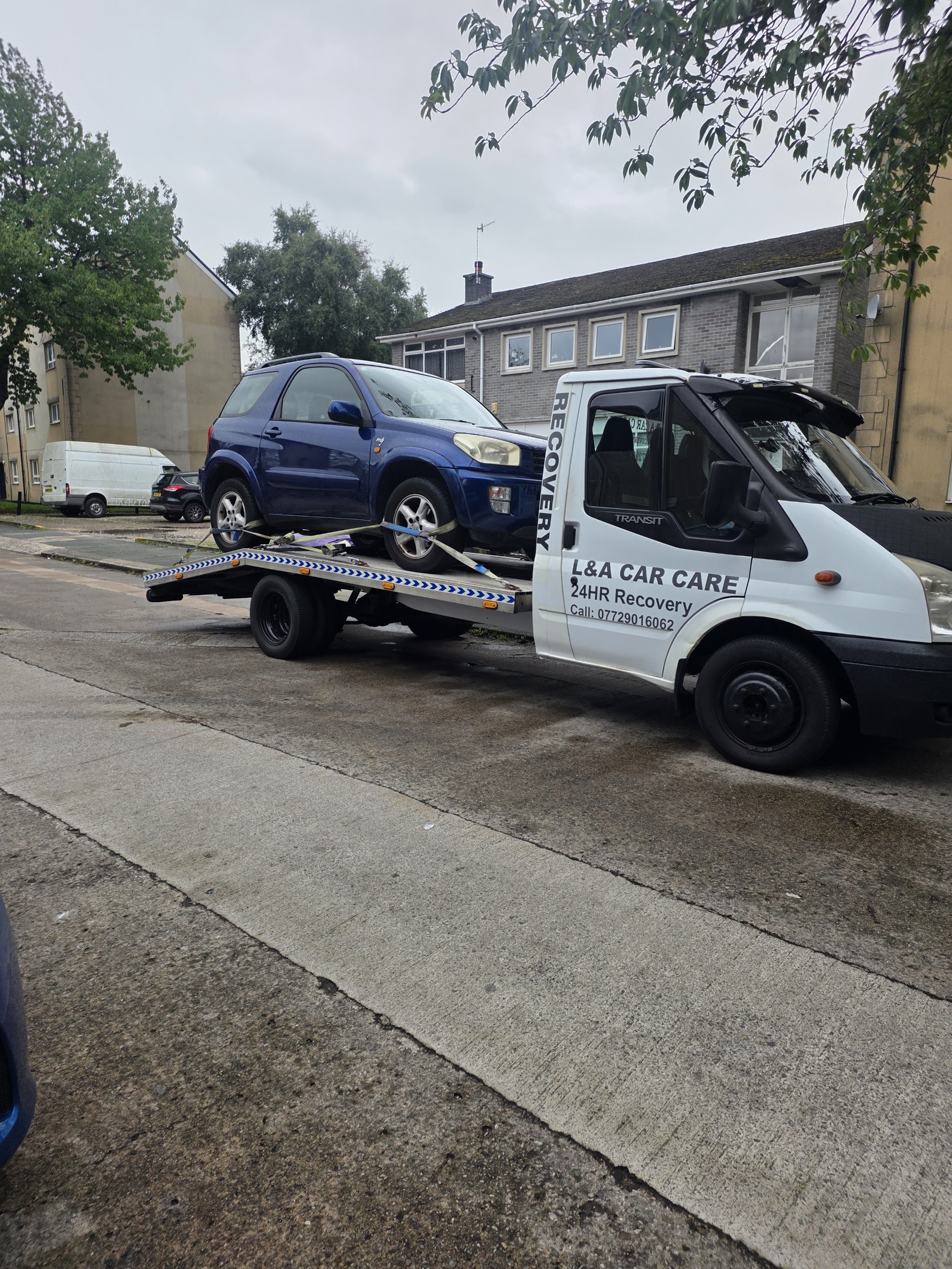 The white L&A Car Care recovery truck with 24HR Recovery on the cab door, carrying a blue car