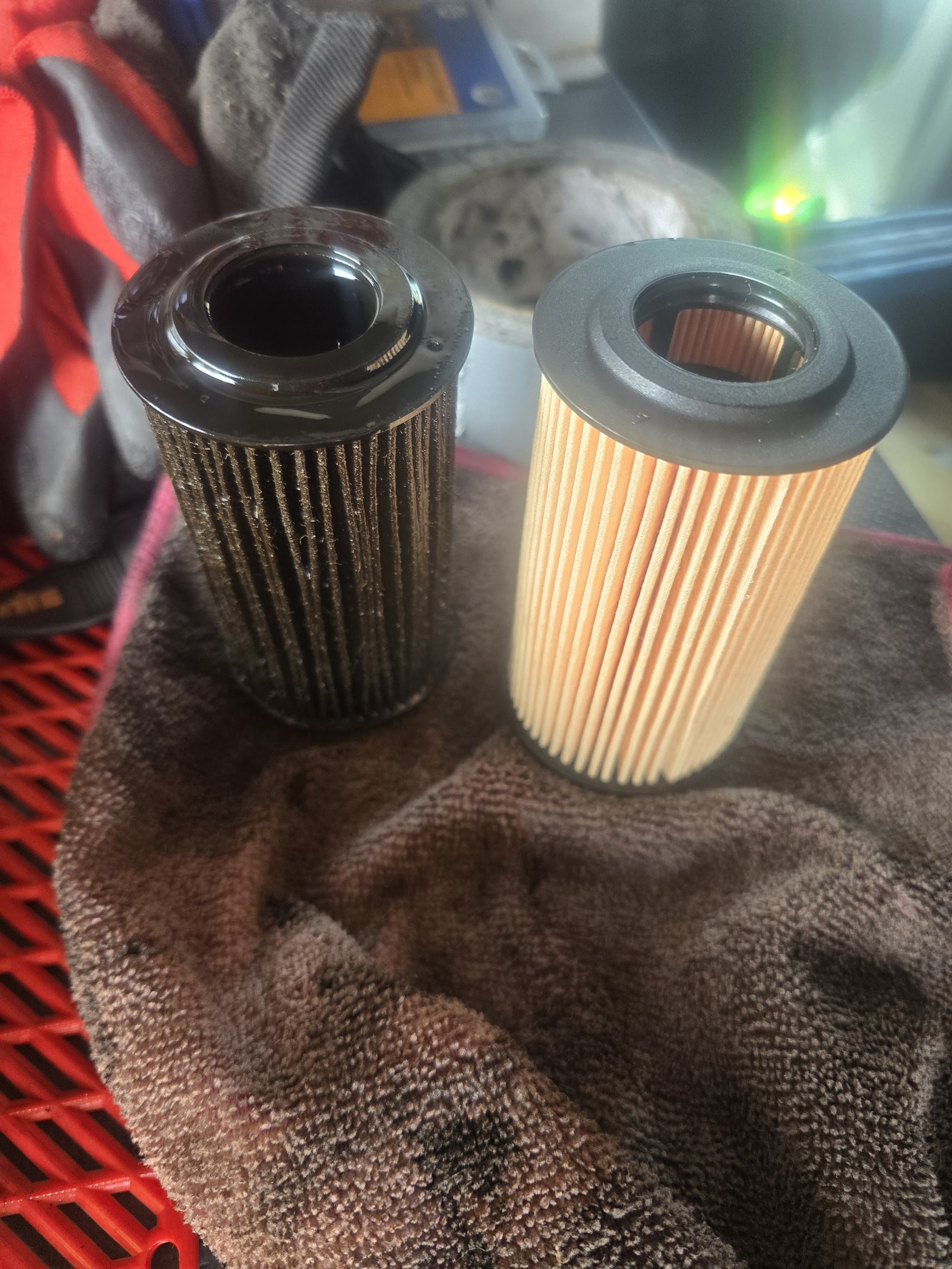 An old dirty oil filter beside a new clean one on a rag