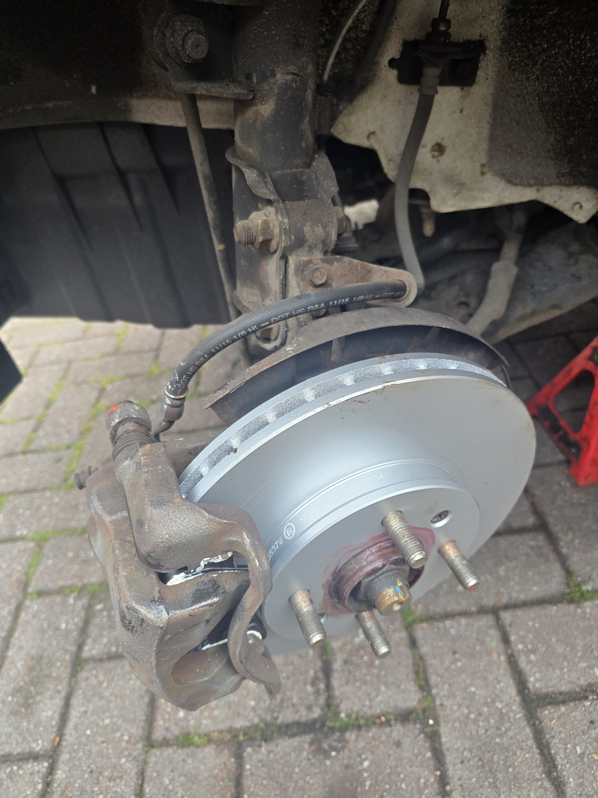 A brake disc and caliper fitted with the wheel off, on block paving