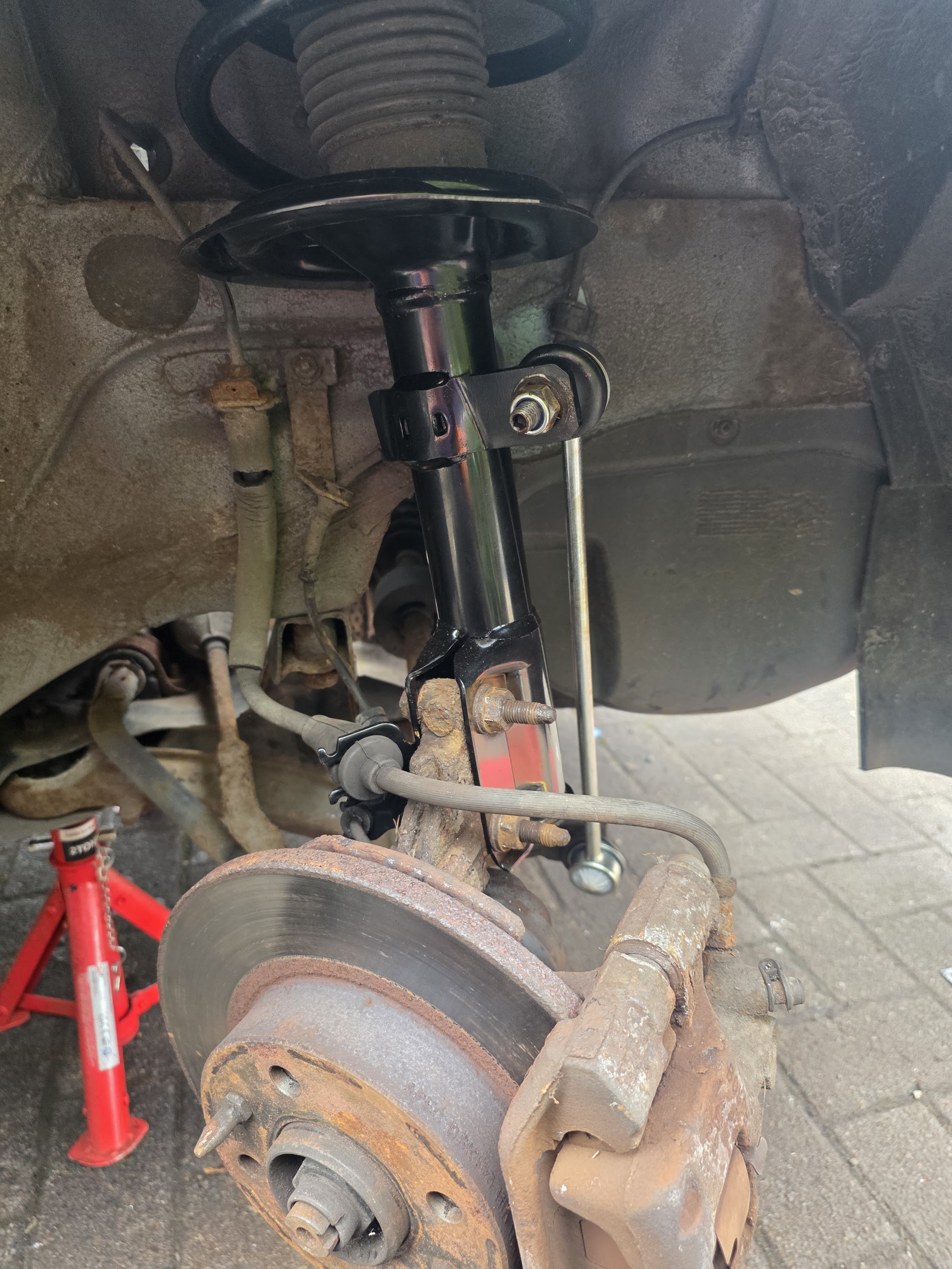 Wheel off and the front corner of a car on an axle stand on a block-paved drive