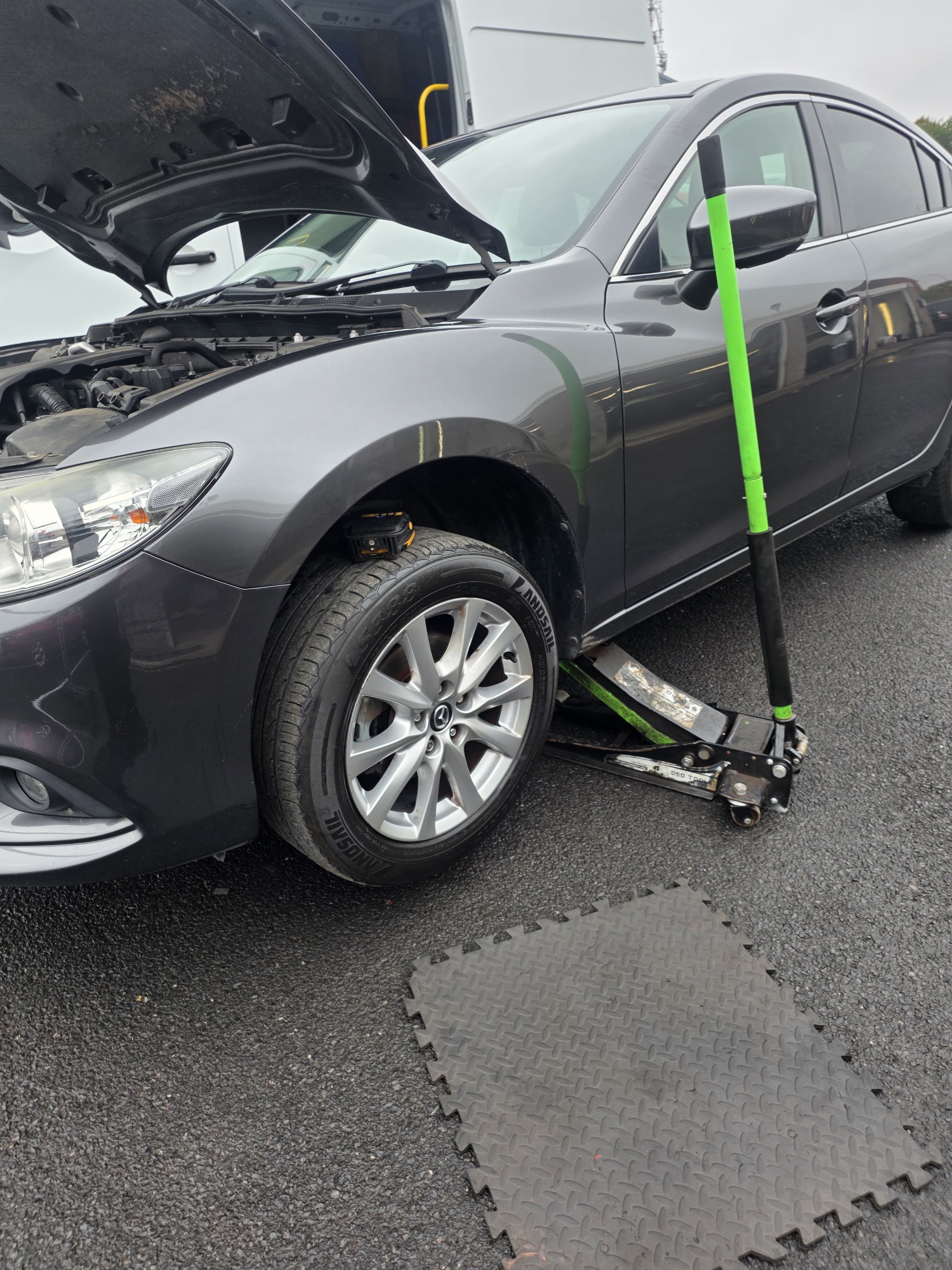 A grey Mazda raised on a trolley jack with the bonnet up, ready for work